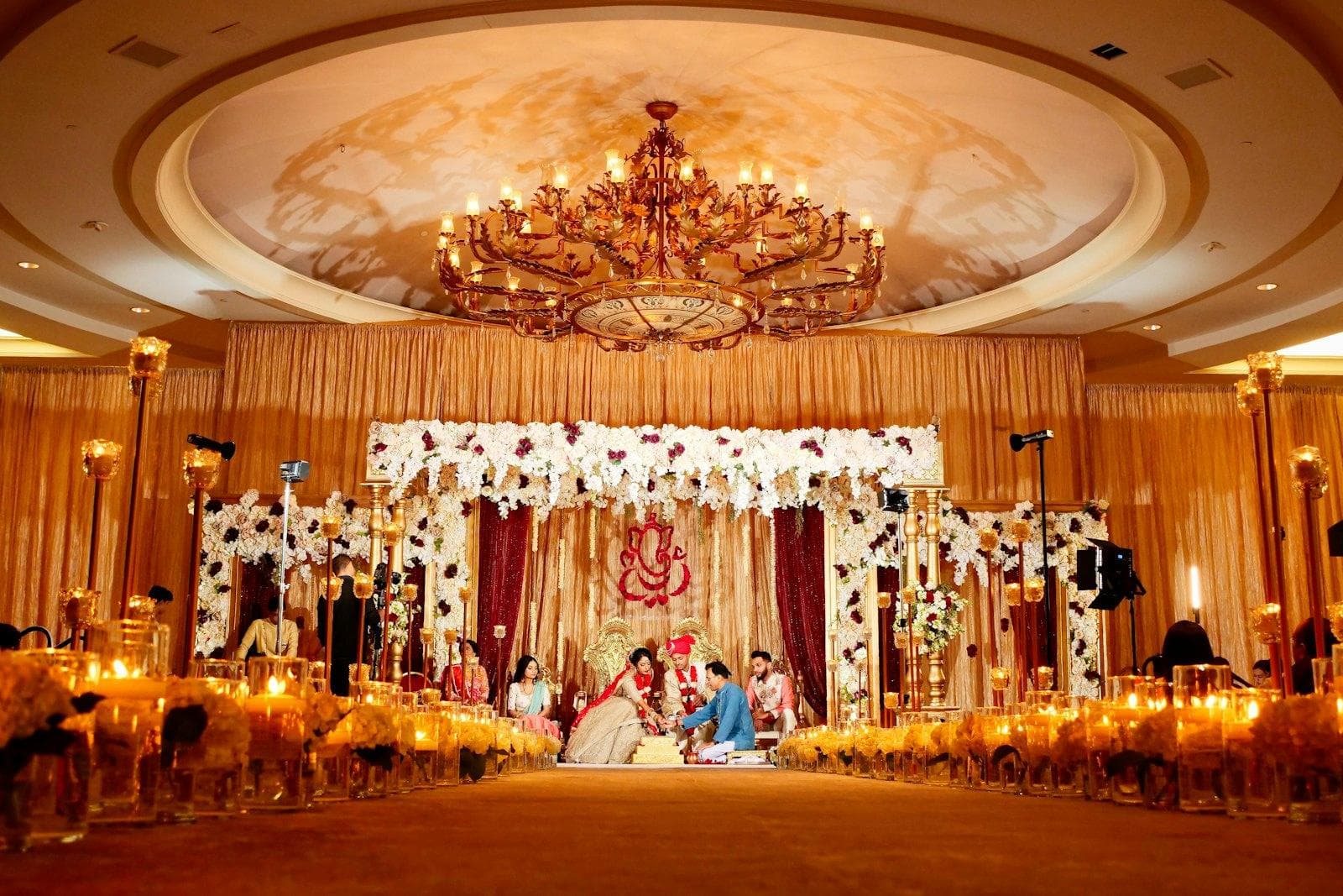 A grand reception hall with a floral mandap and chandeliers